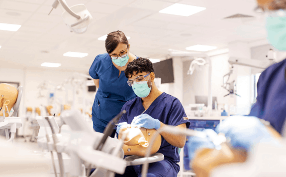 A clinician demonstrates practical skills to a student while working on a phantom head